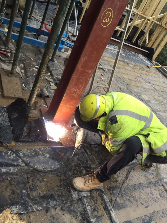 A welder in hi-vis working on a steel beam in a basement excavation