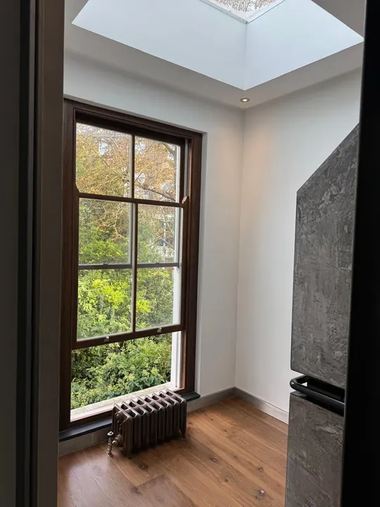 A bright finished basement-level room with a sash window and a skylight above