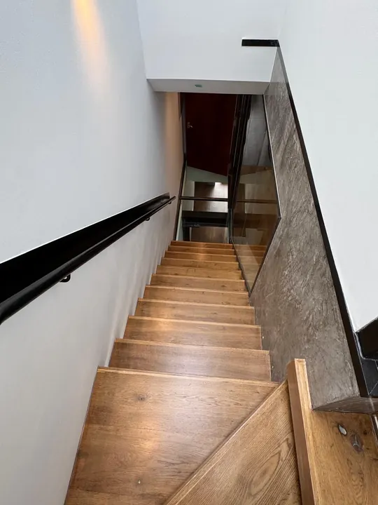 A finished oak staircase with a black handrail leading down to a basement