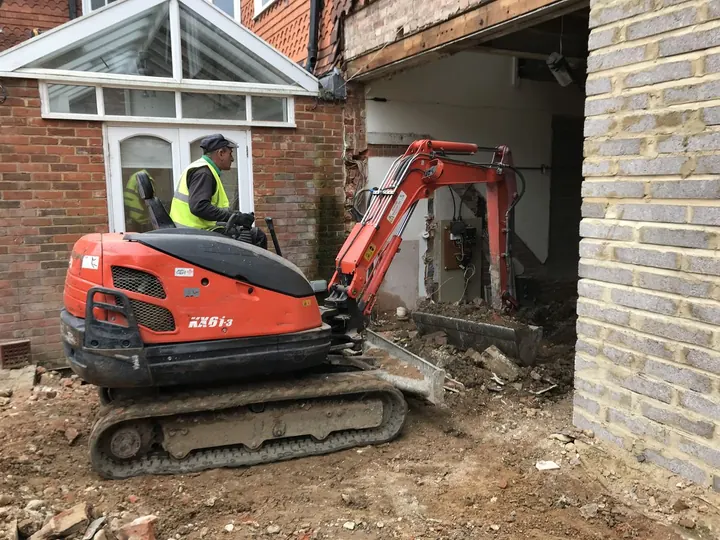 A mini excavator working beside a brick house to dig out a new basement