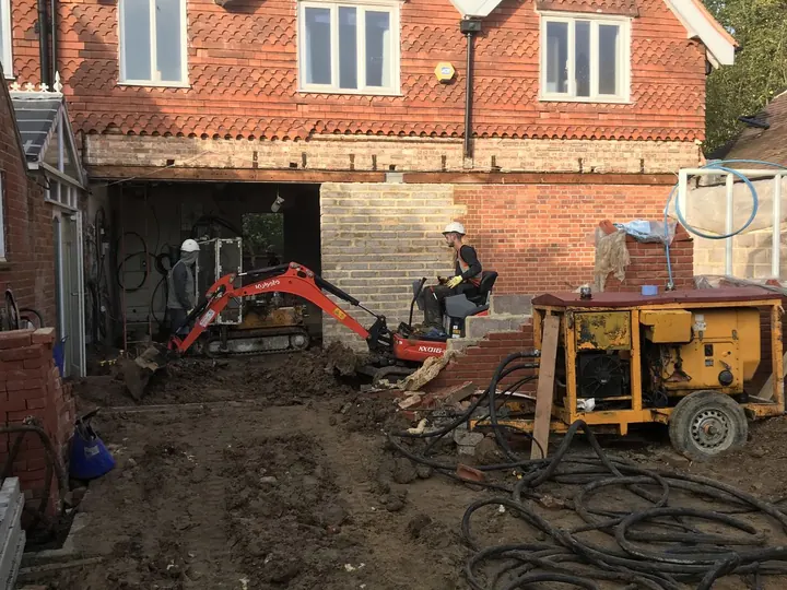 A mini excavator and pump at the rear of a brick house during basement excavation